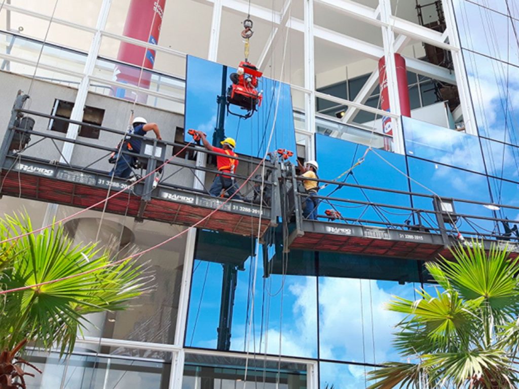 Trabalhadores implantando fachada de vidro temperado